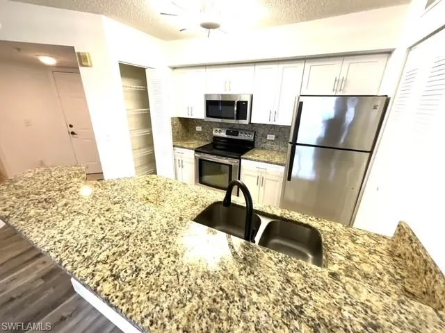 Kitchen featuring appliances with stainless steel finishes, white cabinets, and light stone countertops