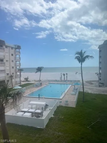 Community pool featuring view of water and beach, a fenced backyard, and a patio