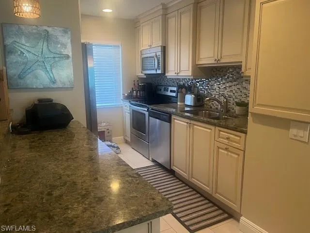 Kitchen with light tile patterned floors, dark stone counters, appliances with stainless steel finishes, and backsplash