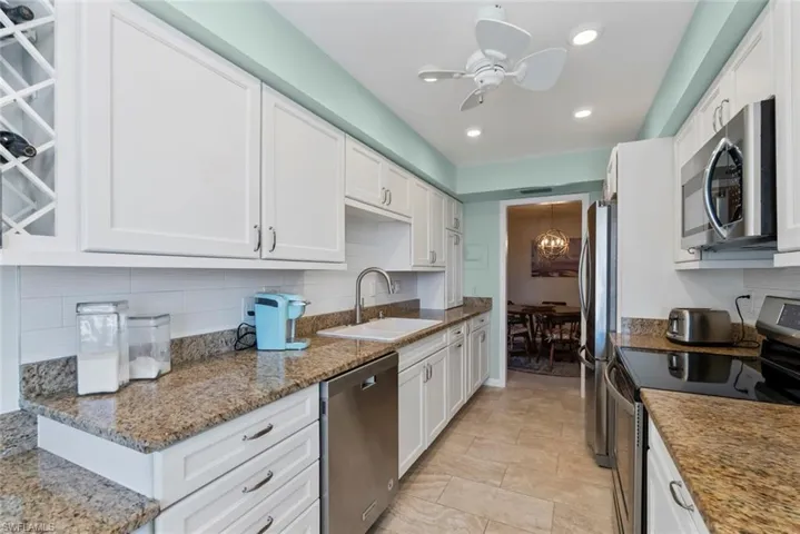 Kitchen featuring stainless steel appliances, tasteful backsplash, white cabinets, light stone countertops, and recessed lighting