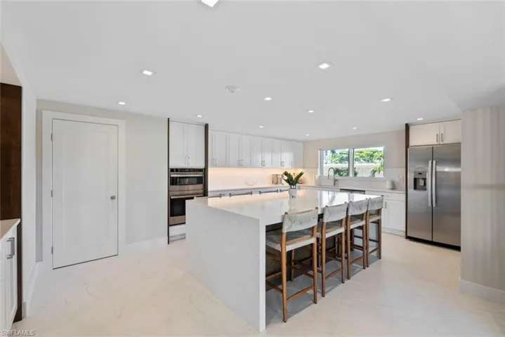 Kitchen featuring a kitchen breakfast bar, appliances with stainless steel finishes, light stone counters, white cabinetry, and light marble finish floors