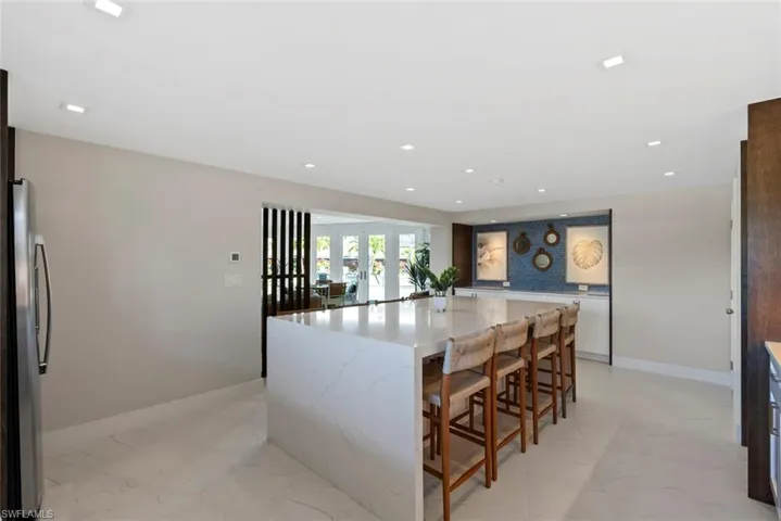 Kitchen featuring light marble finish flooring, recessed lighting, freestanding refrigerator, a kitchen breakfast bar, and light stone countertops