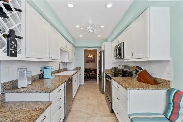 Kitchen with tasteful backsplash, stainless steel appliances, light stone countertops, white cabinets, and recessed lighting