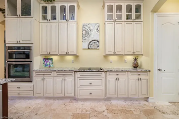 Kitchen featuring double wall oven, light stone counters, and black downdraft cooktop