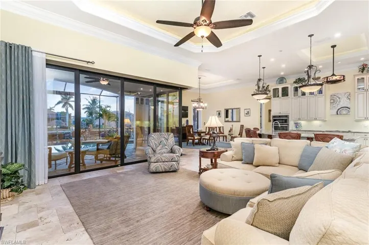 Living speca featuring ceiling fan with notable chandelier, a tray ceiling, and crown molding