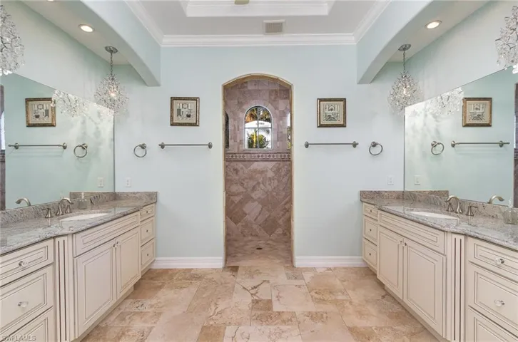 Maater bathroom featuring a walk in shower, dual vanities, chandeliers and ornamental molding