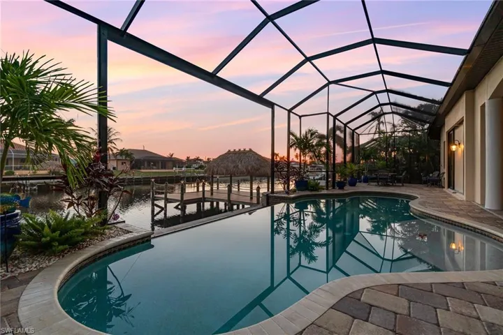 Pool at dusk featuring a boat dock, a patio, a water view, and screen enclosure