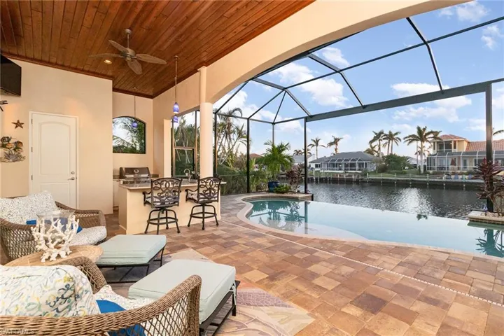 View of lanai with a water view clearly visible through panoramic screen, wood panel ceiling with fan outdoor kitchen