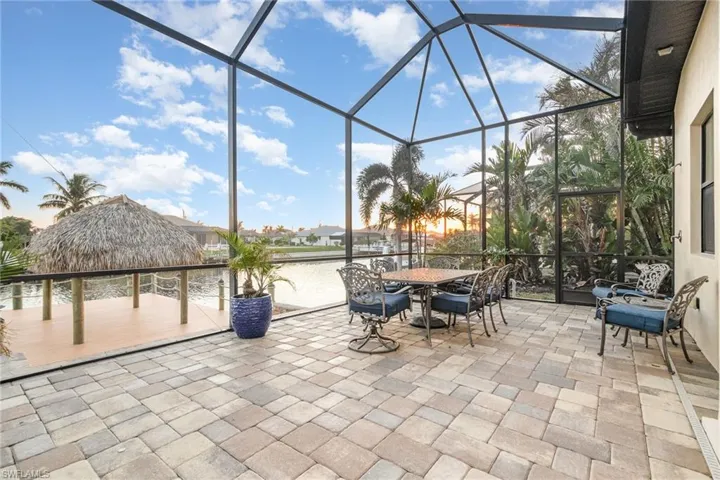 Extened paver patio under pool cage with view of tiki hut and a water view