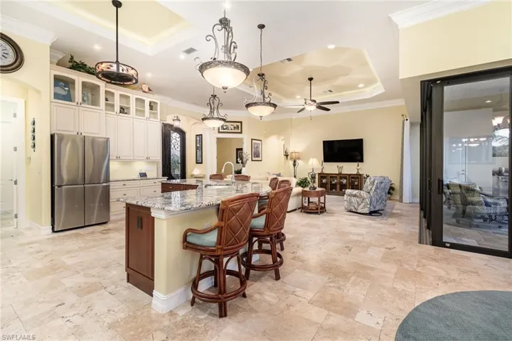Kitchen with upgraded stainless steel fridge, ceiling fan, hanging light fixtures, and the large curved island and nice view of the french pattern travertine flooring