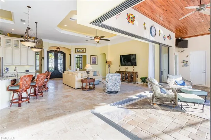 Living space with ceiling fan, ornamental molding, a tray ceiling, and 90 degree sliding impact doors bring outdoor living in. Note wood panel ceiling in lanai