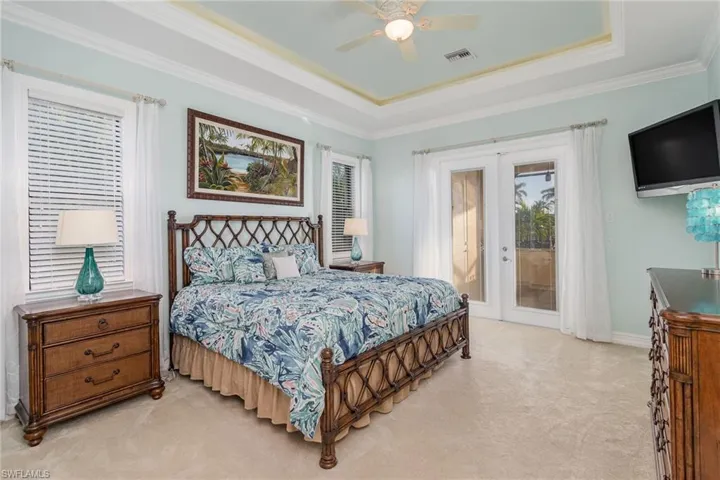 Master Bedroom featuring ceiling fan, french doors giving access to lanai, light colored carpet, tray ceilings and new Tommy Bahama bedroom set