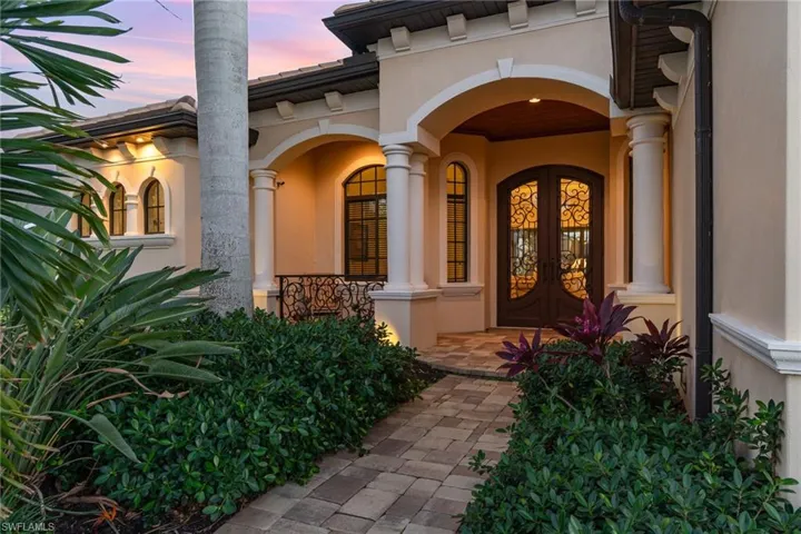 Exterior entry at dusk featuring iron french doors and lush landscaping