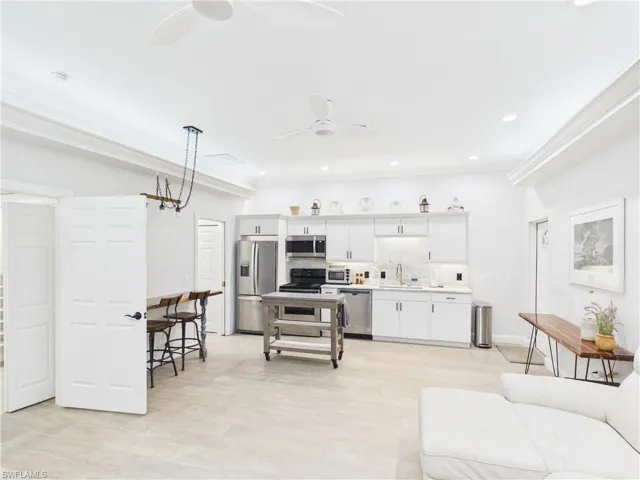 Open-concept living space featuring a modern kitchen with stainless steel appliances, white cabinetry, and a light-toned backsplash