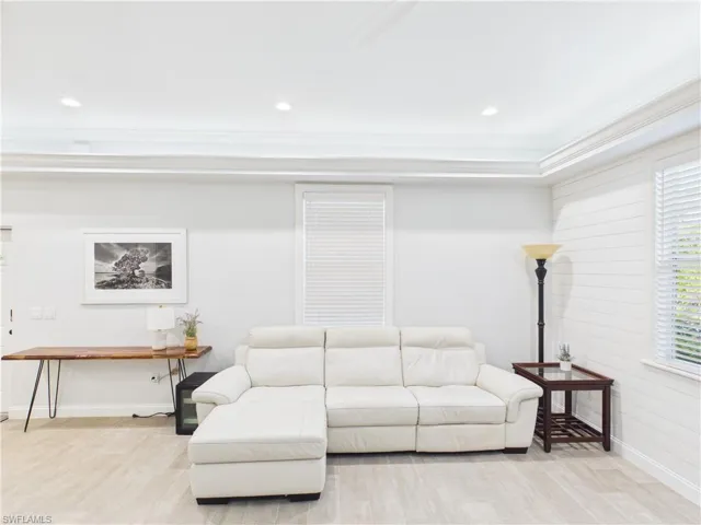 Recessed lighting illuminates this bright space featuring a tray ceiling with crown molding, light wood-finish flooring, and white horizontal wall paneling