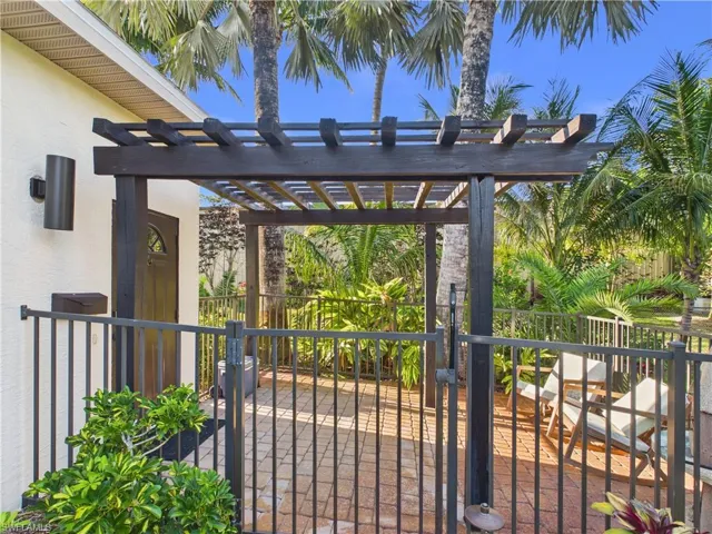 Covered patio featuring a dark wood pergola, black metal fencing, and paver flooring