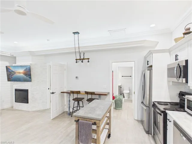 Open-concept living area featuring a corner fireplace with white stone surround, a ceiling fan, and light wood-finish flooring