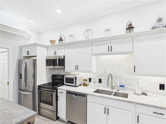 Modern kitchen featuring white cabinetry with matte black hardware, stainless steel appliances, a double basin sink, and light stone countertops