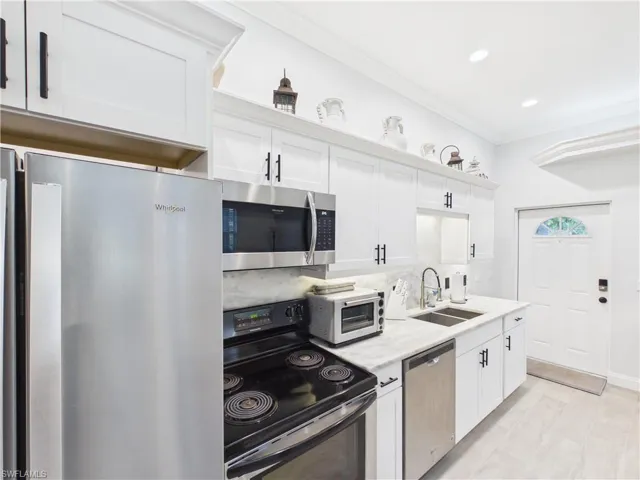 Kitchen featuring white cabinetry with dark hardware, stainless steel appliances, a double basin sink, and light-toned flooring