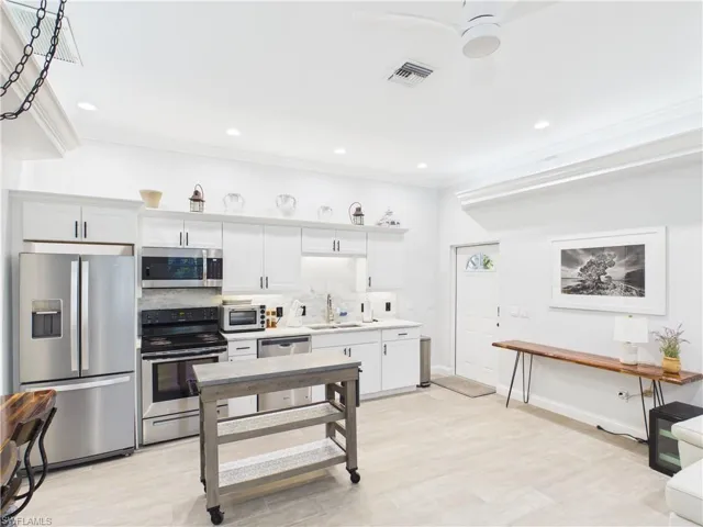Bright kitchen featuring white cabinetry, stainless steel appliances, light-toned flooring, recessed lighting, and crown molding