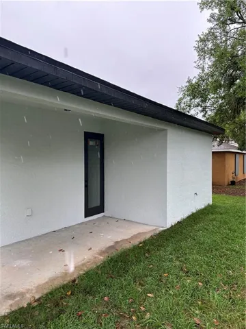 Rear view of house with stucco siding, a lawn, and a patio