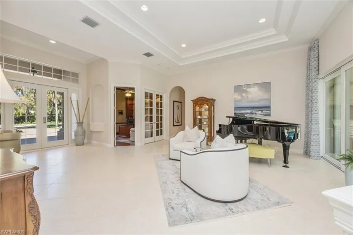Living room with french doors, arched walkways, a raised ceiling, recessed lighting, and ornamental molding