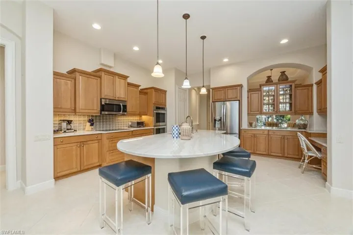 Kitchen featuring a breakfast bar area, glass insert cabinets, tasteful backsplash, hanging light fixtures, and a kitchen island with sink