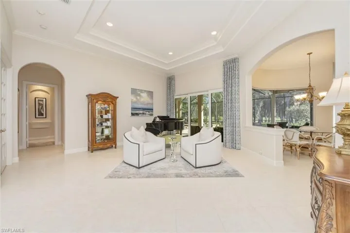 Living area with arched walkways, a chandelier, crown molding, a tray ceiling, and recessed lighting