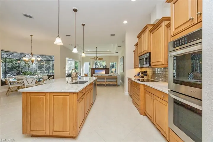 Kitchen featuring appliances with stainless steel finishes, light stone counters, hanging light fixtures, decorative backsplash, and a center island with sink