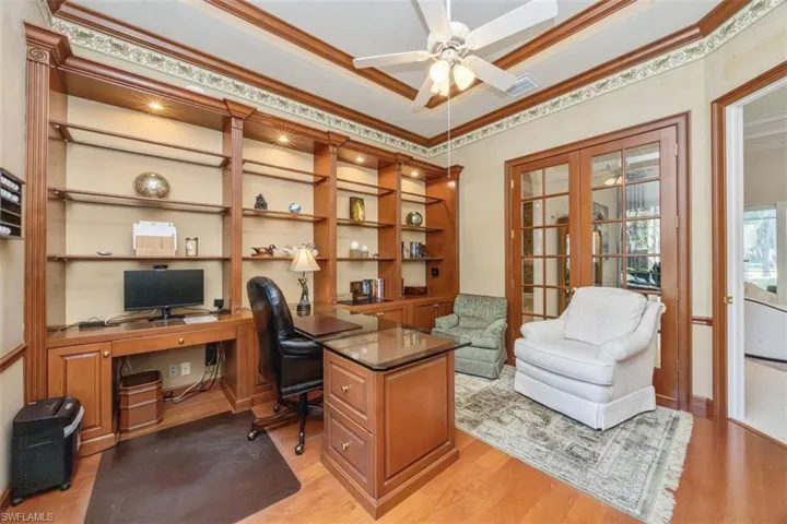 Office area featuring ornamental molding, light wood-style floors, a tray ceiling, and a ceiling fan