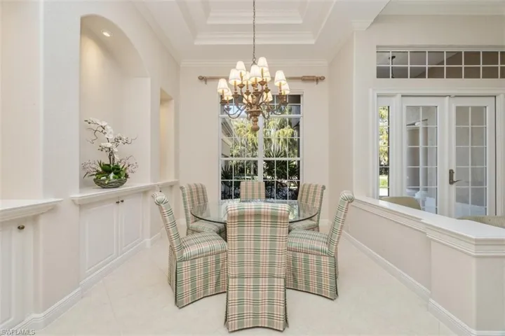 Dining space with crown molding, a tray ceiling, a chandelier, french doors, and tile patterned floors