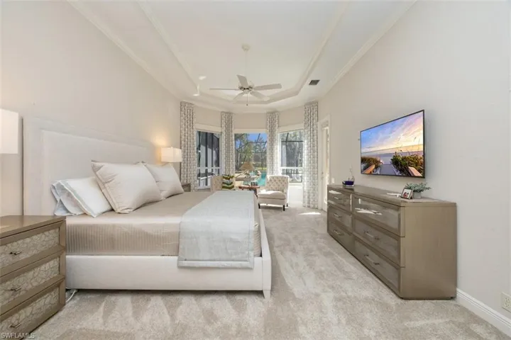 Bedroom featuring a tray ceiling, light carpet, a ceiling fan, and ornamental molding