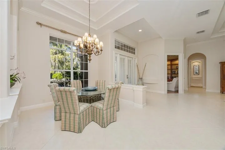 Dining area featuring ornamental molding, arched walkways, light tile patterned floors, a chandelier, and a raised ceiling