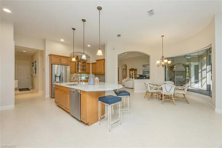 Kitchen with glass insert cabinets, brown cabinetry, a chandelier, arched walkways, and a spacious island
