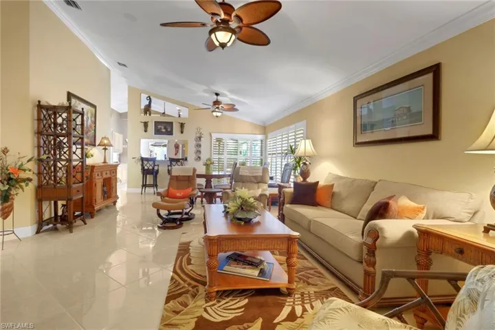 Living room with ceiling fan, light tile patterned floors, lofted ceiling, and ornamental molding