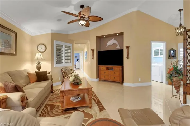 Living room featuring ceiling fan with notable chandelier, vaulted ceiling, light tile patterned floors, crown molding, and washer / clothes dryer