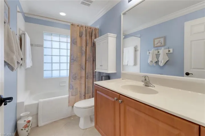 Full bathroom with tile patterned flooring, shower / bath combination with curtain, vanity, crown molding, and toilet