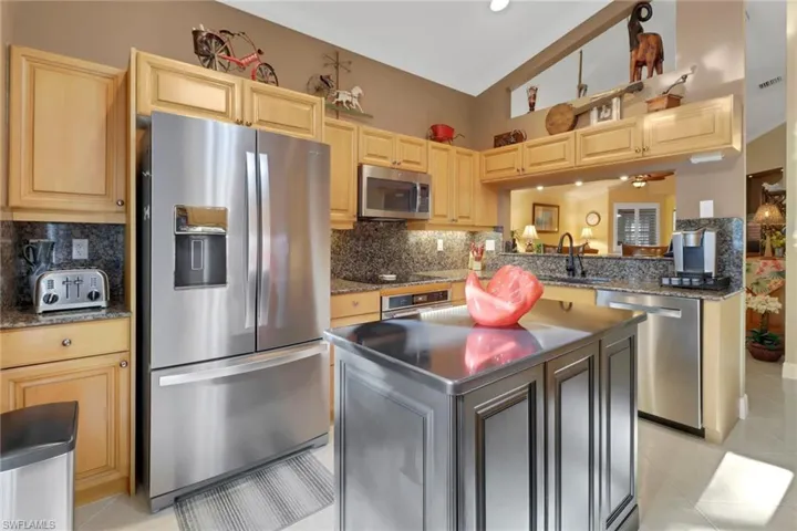 Kitchen featuring stainless steel appliances, light tile patterned floors, vaulted ceiling, a center island, and decorative backsplash