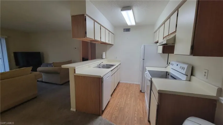 Kitchen with white appliances, light hardwood / wood-style floors, white cabinetry, sink, and a textured ceiling