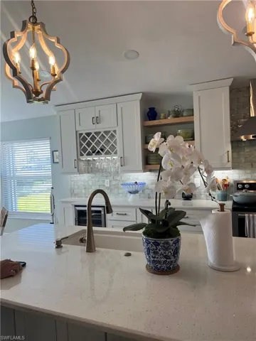 Kitchen with hanging lights, light stone countertops, white cabinets, and black range
