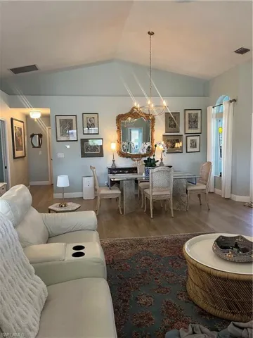 Living room with hanging lights, wood finished floors, and lofted ceiling
