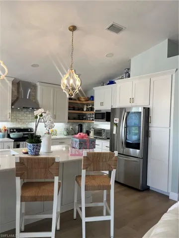 Kitchen with white cabinetry, stainless steel appliances, dark wood-style floors, and lofted ceiling