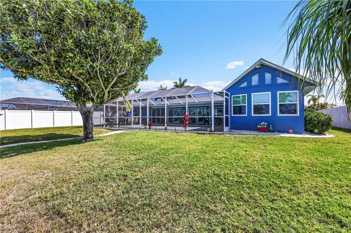 Expansive screened lanai with a covered patio, complemented by a large grassy yard featuring a mature tree