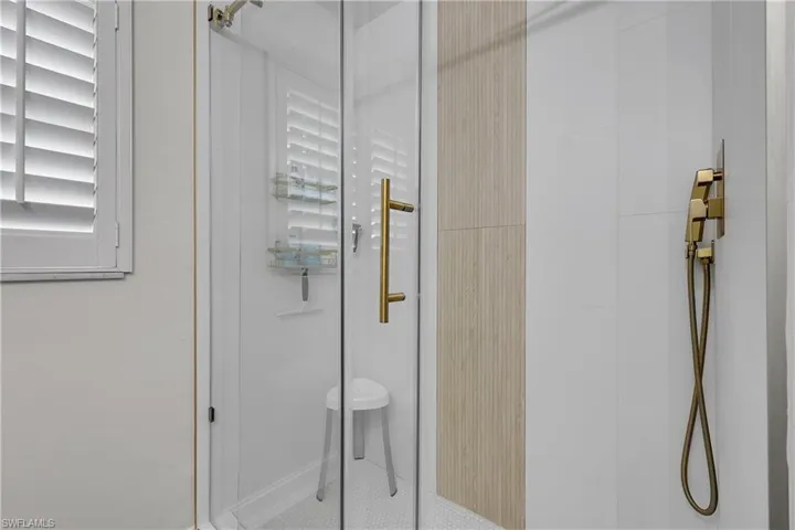 Glass-enclosed shower featuring a gold-toned handle, white hexagonal floor tiles, and a vertical wood-look accent panel