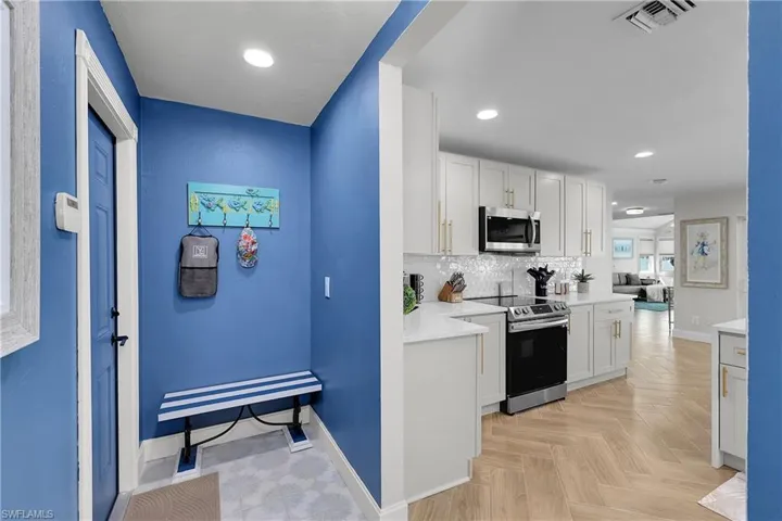 Contemporary kitchen featuring white cabinetry, stainless steel appliances, and herringbone-pattern wood-finish flooring