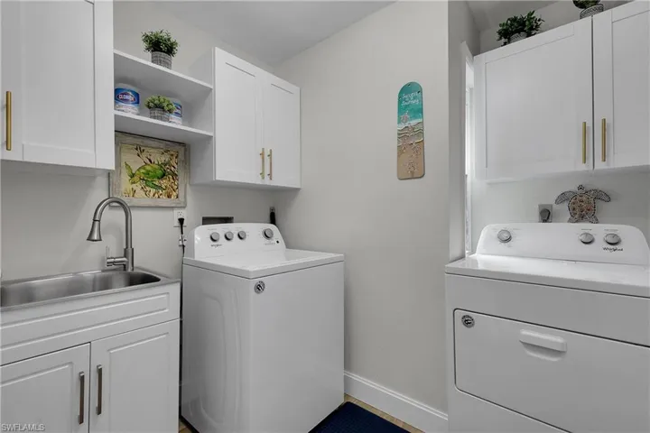 Dedicated laundry area featuring white cabinetry with gold-toned hardware, a stainless steel utility sink with a pull-down faucet, and built-in shelving