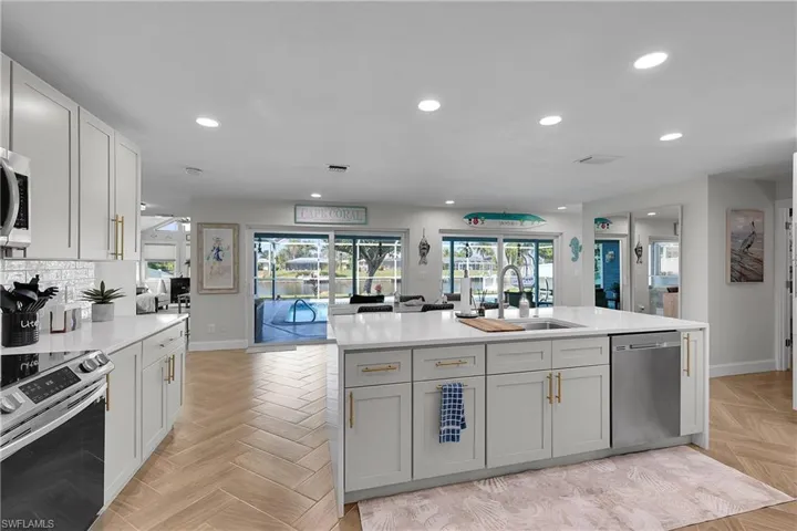 Kitchen featuring an island with an undermount sink, stainless steel dishwasher, and white cabinetry with gold-tone hardware
