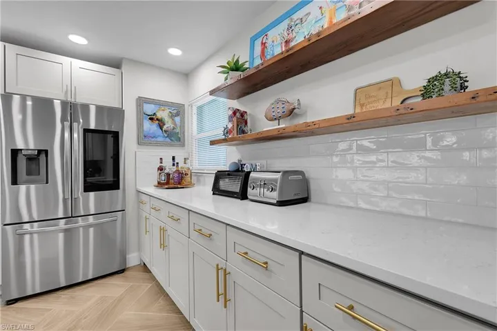 Modern kitchen featuring light gray cabinetry with gold-toned hardware, solid surface countertops, and an elongated subway tile backsplash