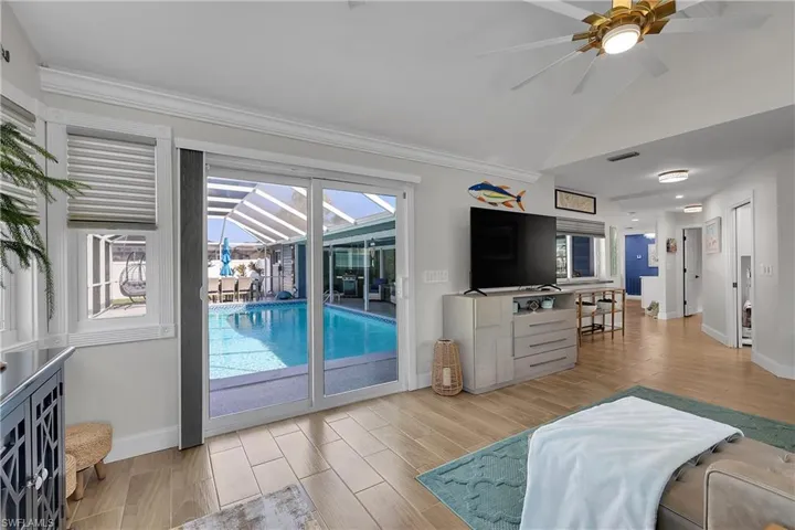Spacious living area featuring large format tile flooring, a vaulted ceiling, and sliding glass doors providing access to the screened pool area