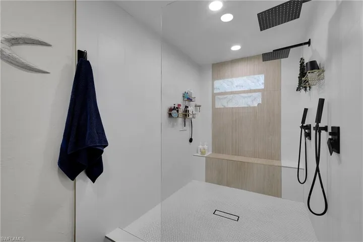 Walk-in shower featuring a glass enclosure, white penny tile flooring, a built-in bench, and a dual matte black shower system with a rain shower head
